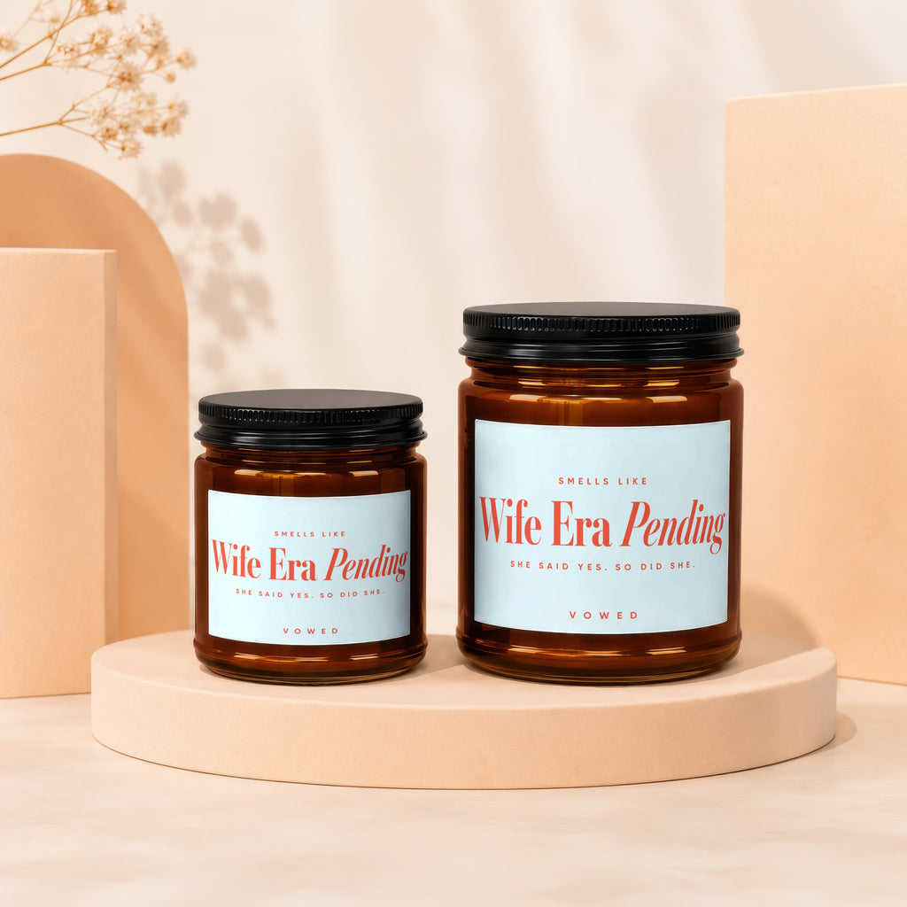 Two amber glass candles with "Wife Era Pending" labels sit on peach pedestals.