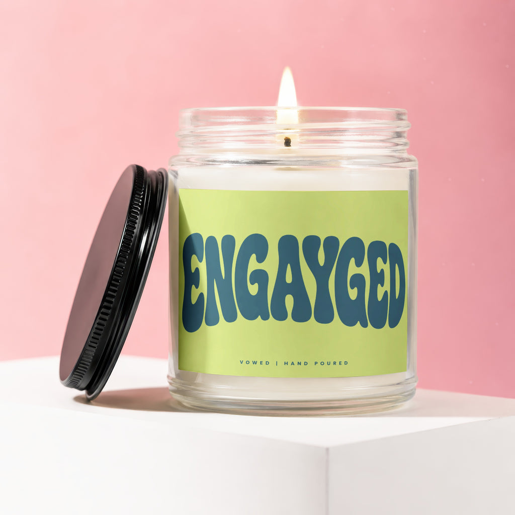 Candle with "ENGAYGED" text on a light green label, Vowed | Hand Poured.