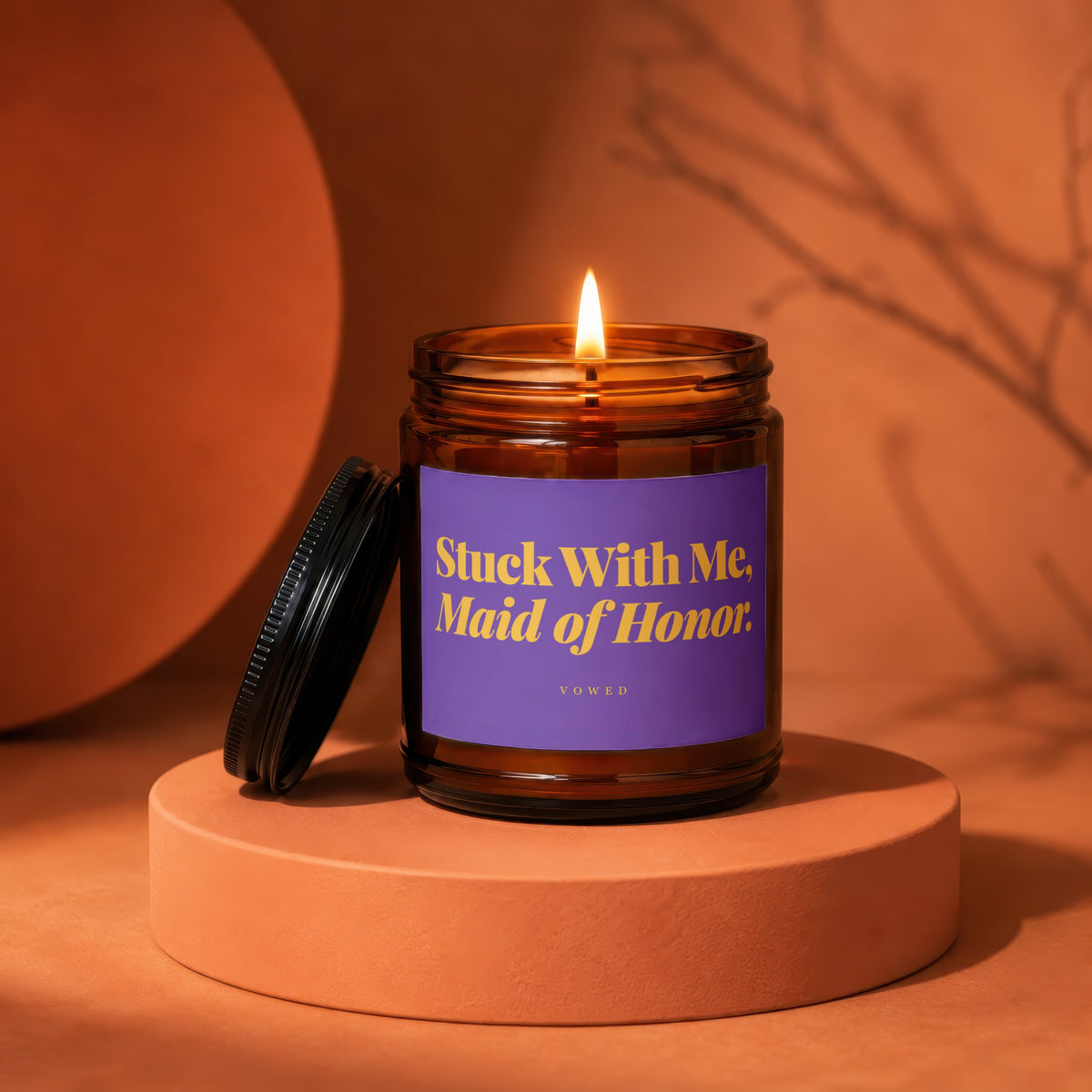 Amber candle with a lit flame and a purple label reading "Stuck With Me, Maid of Honor."