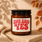 Amber jar candle with "SHE SAID YES" and "VOWED" text on a cream label.
