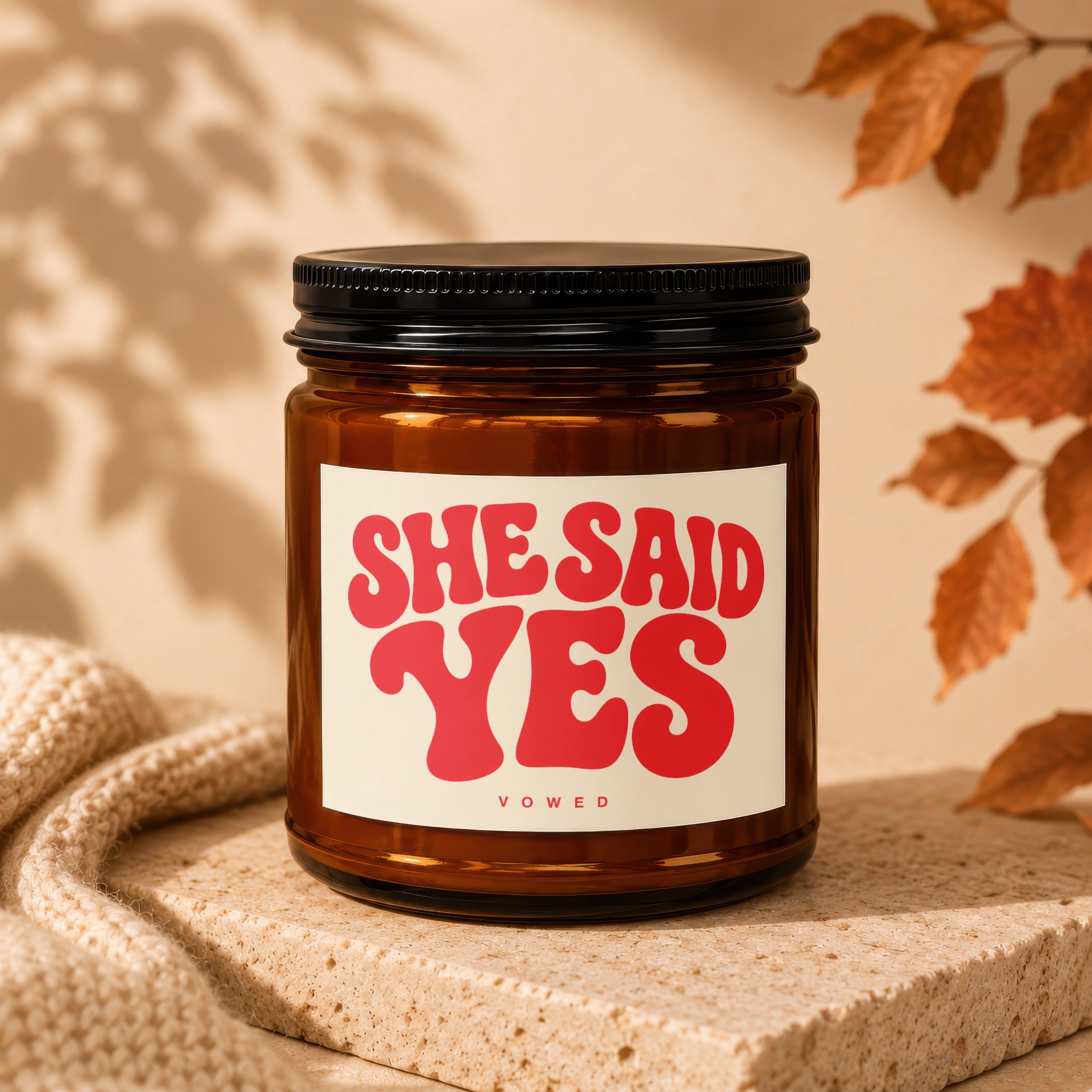 Amber jar candle with "SHE SAID YES" and "VOWED" text on a cream label.