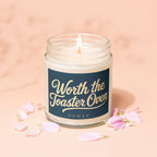 Lit candle in a jar with navy label reading "Worth the Toaster Oven VOWED".