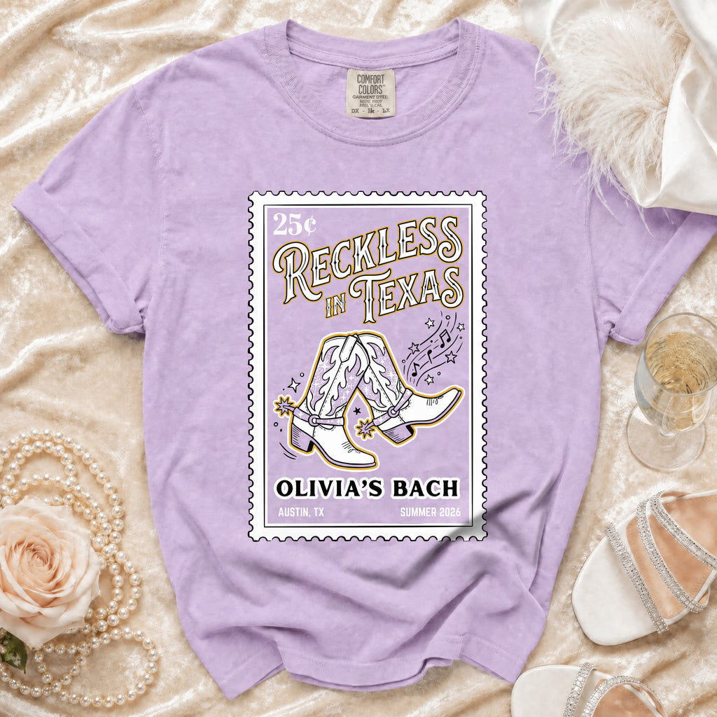Purple t-shirt with "Reckless in Texas" graphic featuring cowboy boots.