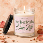 Candle with lit wick and label reading "Smells Like Two Toothbrushes, One Life VOWED."