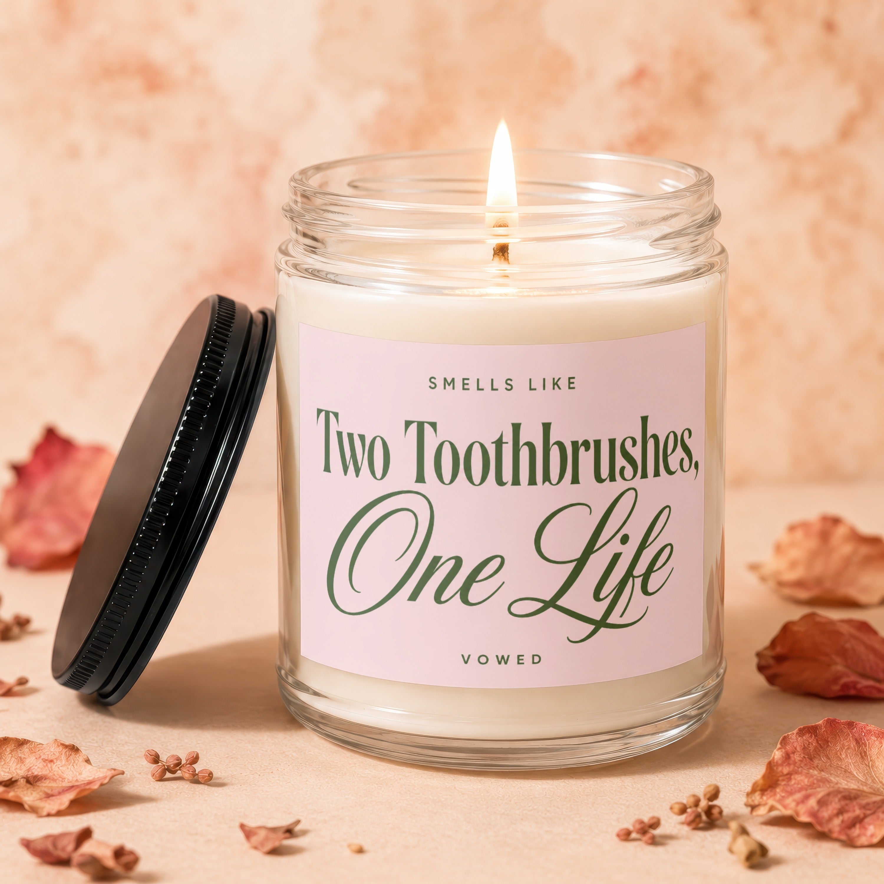 Candle with lit wick and label reading "Smells Like Two Toothbrushes, One Life VOWED."