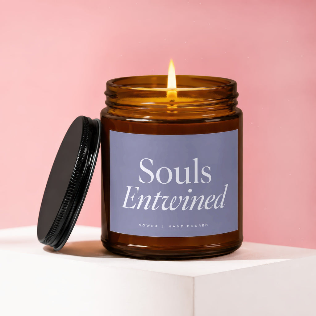 Lit scented candle with label "Souls Entwined, Vowed | Hand Poured" on pink background.