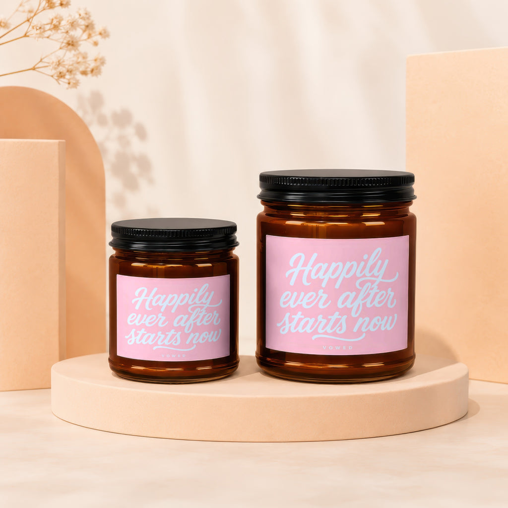 Two amber glass candles with pink labels reading "Happily ever after starts now".