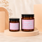 Two amber glass candles with pink labels reading "Happily ever after starts now".