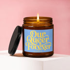 Lit amber glass candle with blue label reading "Our Queer Forever Vowed".