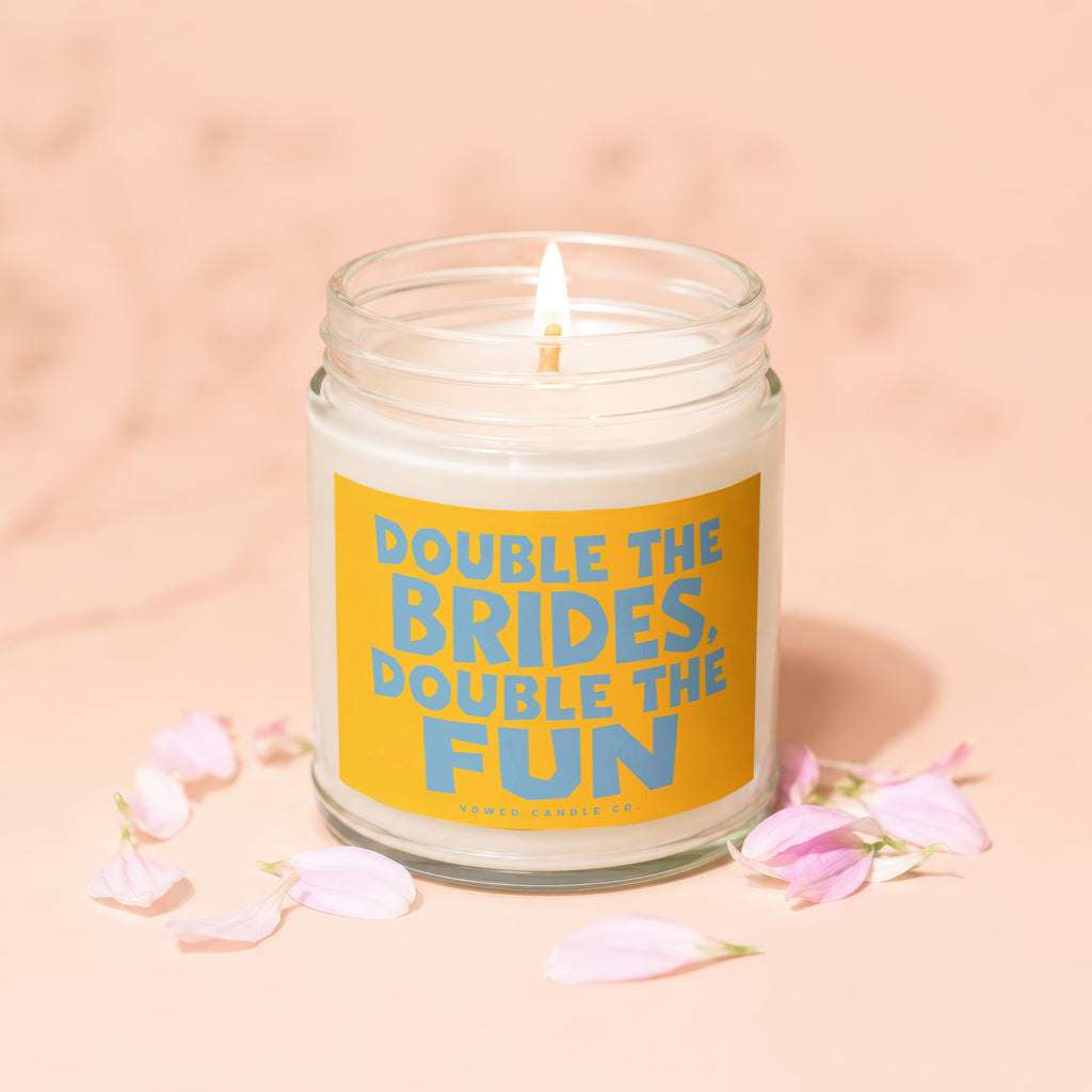 Lit candle in glass jar with yellow label reading "Double the Brides, Double the Fun."