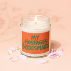 Candle with orange label reading "MY HOSTAGES BRIDESMAIDS VOWED".