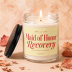 Jar candle with "Maid of Honor Recovery Treatment Ongoing" text, lid detached.