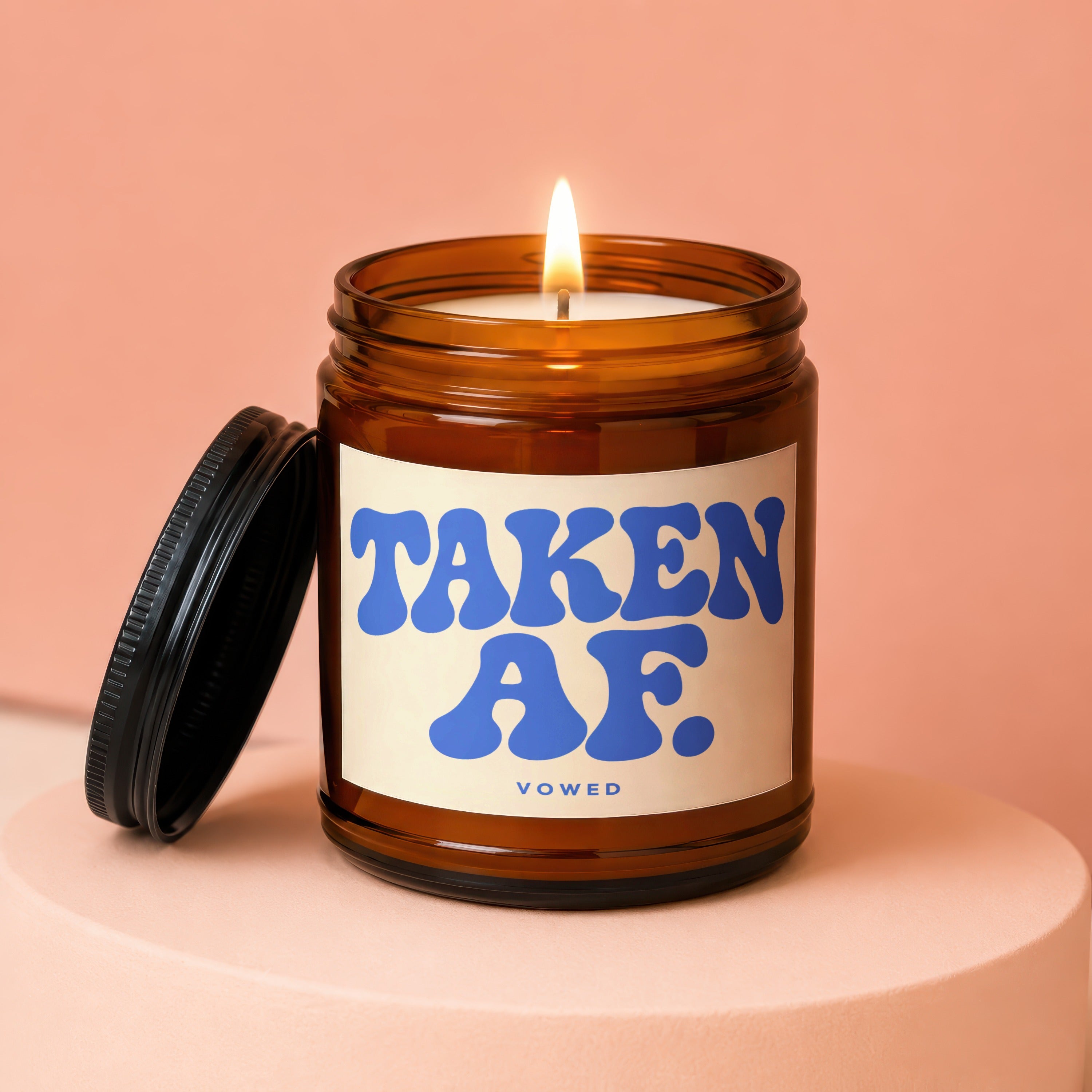 Amber jar candle lit with "TAKEN AF" text on the label and "VOWED" below.