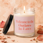 Jar candle with pink label reading "Welcome to the Outlaws In-Laws" and "vowed."