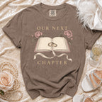 Brown t-shirt with "Our Next Chapter" text, open book, rings, and roses graphic.