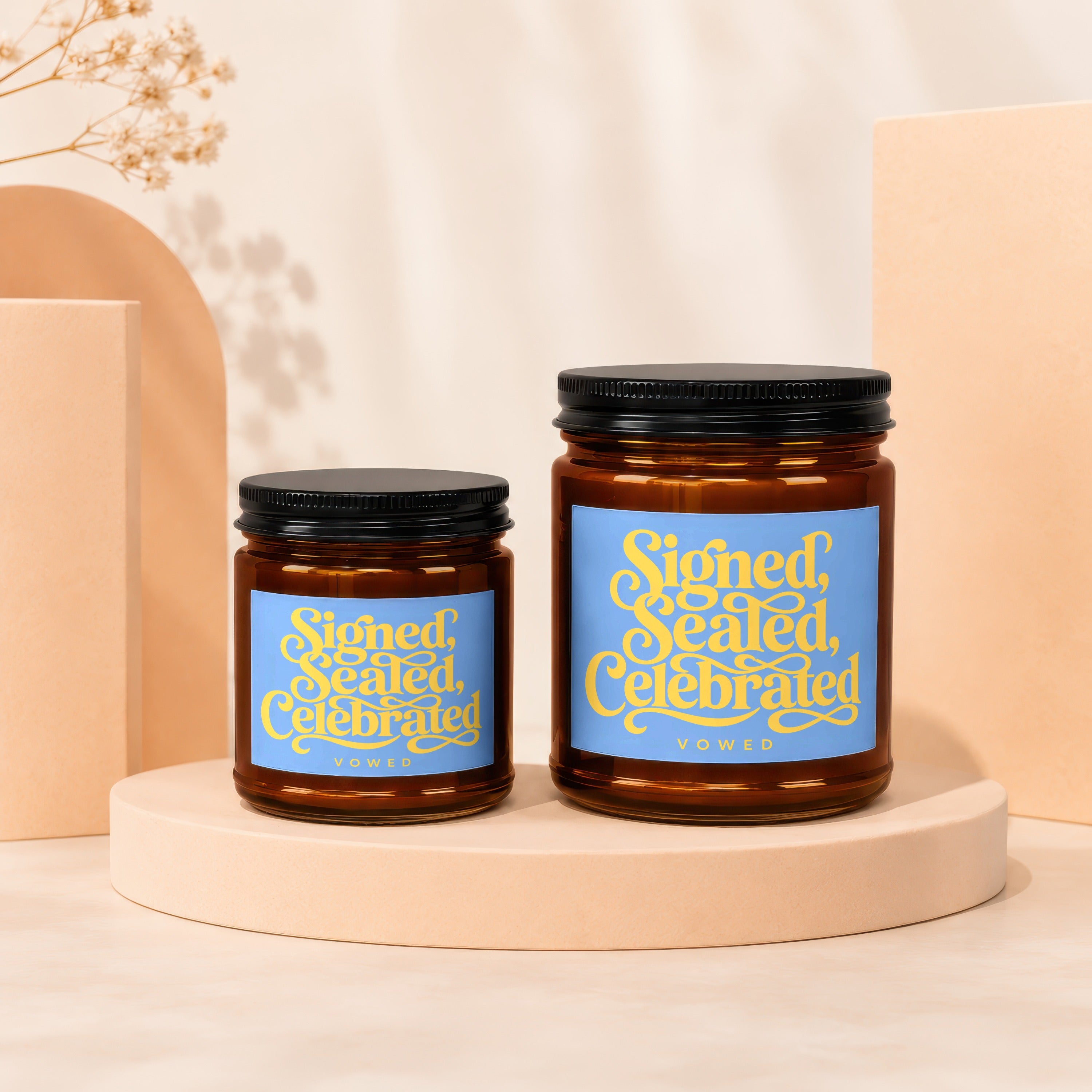 Two amber glass candles with blue labels reading "Signed, Sealed, Celebrated VOWED".