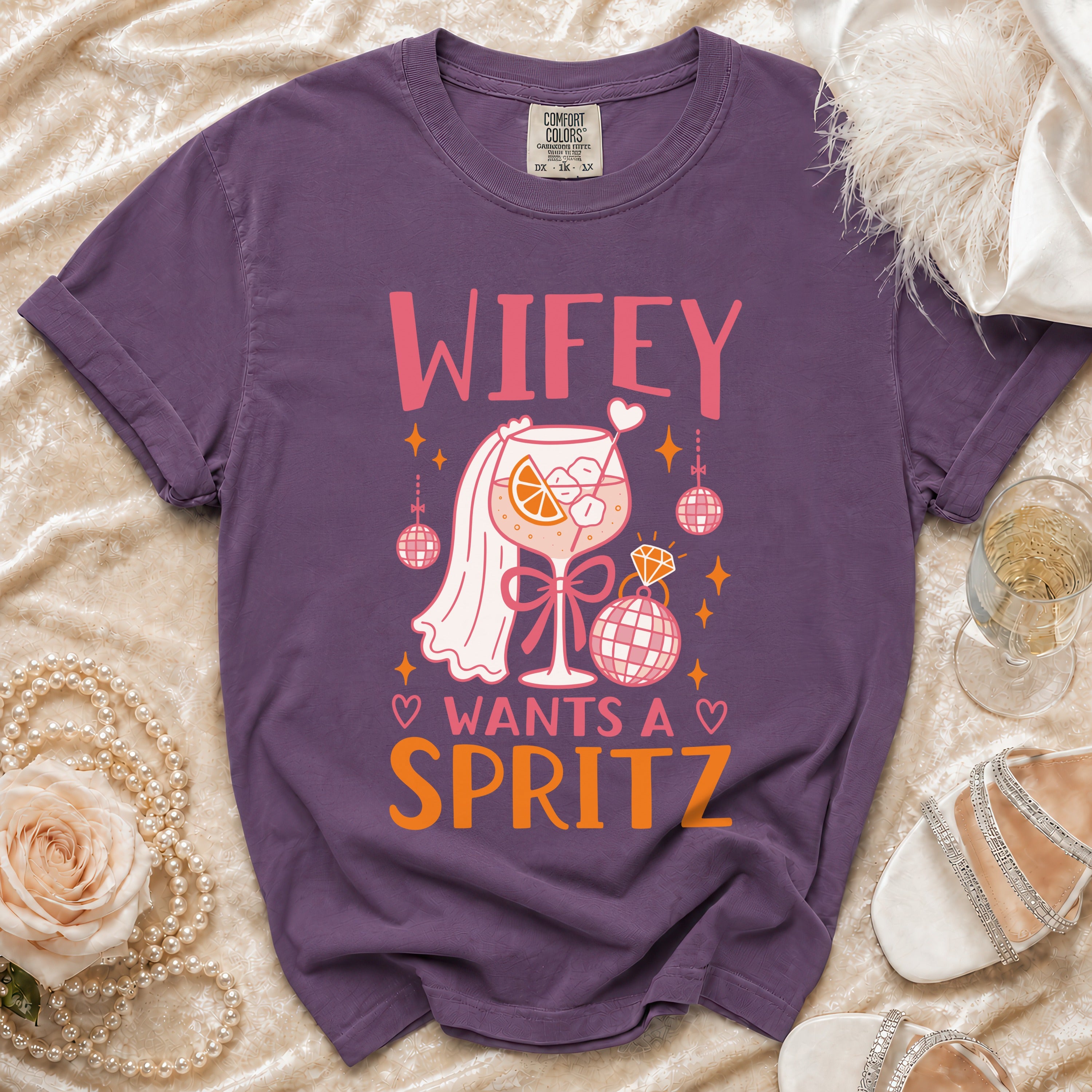 Purple t-shirt with graphic "Wifey Wants A Spritz," cocktail, disco balls, and ring.