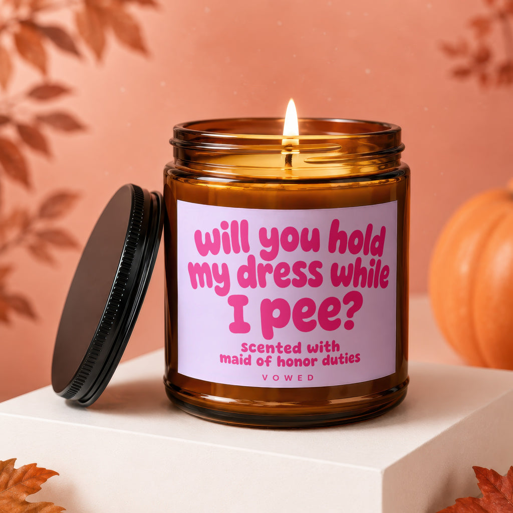 Amber jar candle with pink text "will you hold my dress while I pee? scented with maid of honor duties".