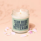 Glass jar candle with lit wick, labeled "Team Bride Recruit Veteran Vowed."