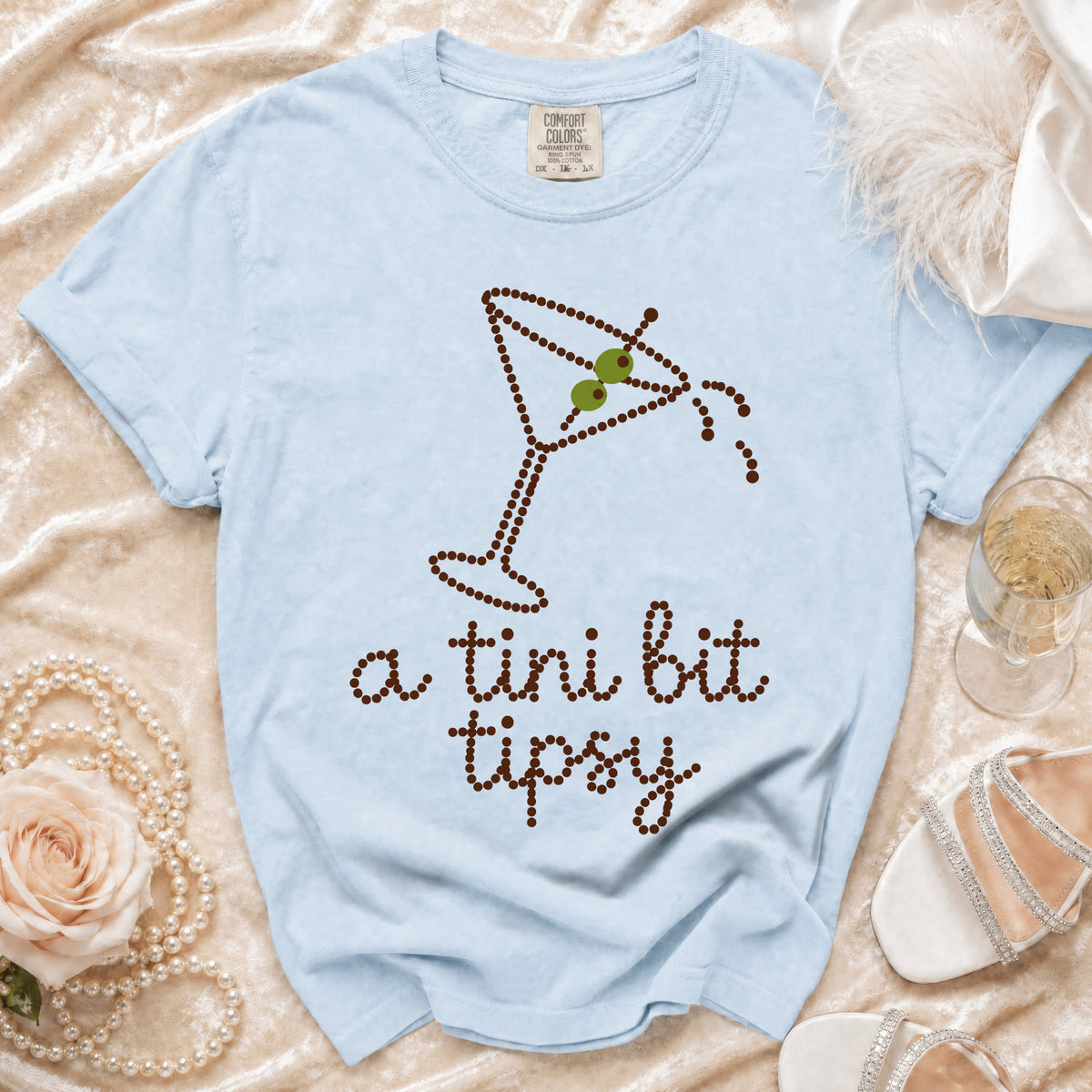 Light blue t-shirt with a dotted martini glass graphic and text "a tini bit tipsy."