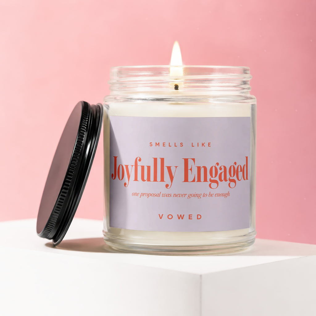Candle with lit wick and black lid, labeled "Joyfully Engaged Vowed".