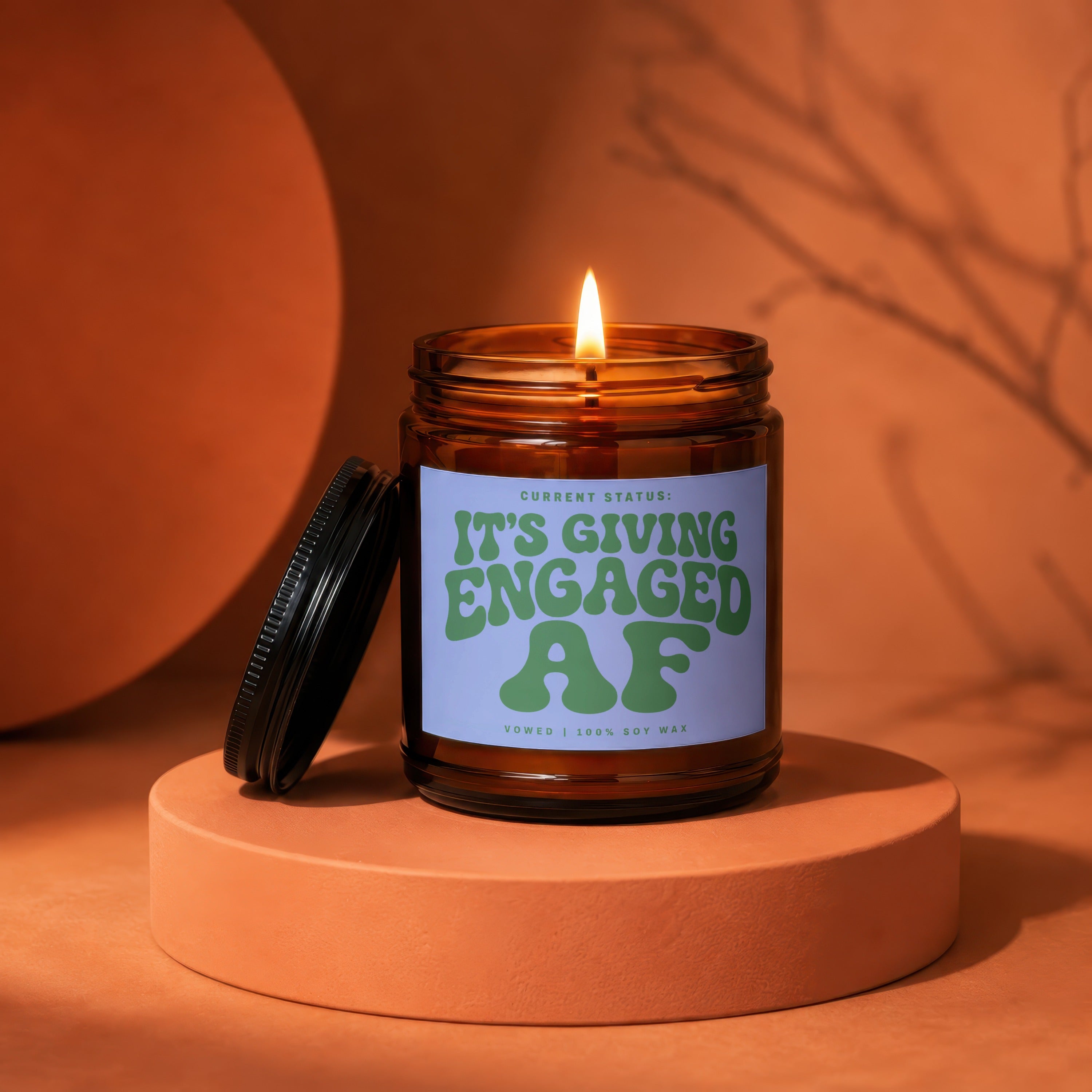 Lit amber glass candle with label reading "IT'S GIVING ENGAGED AF".
