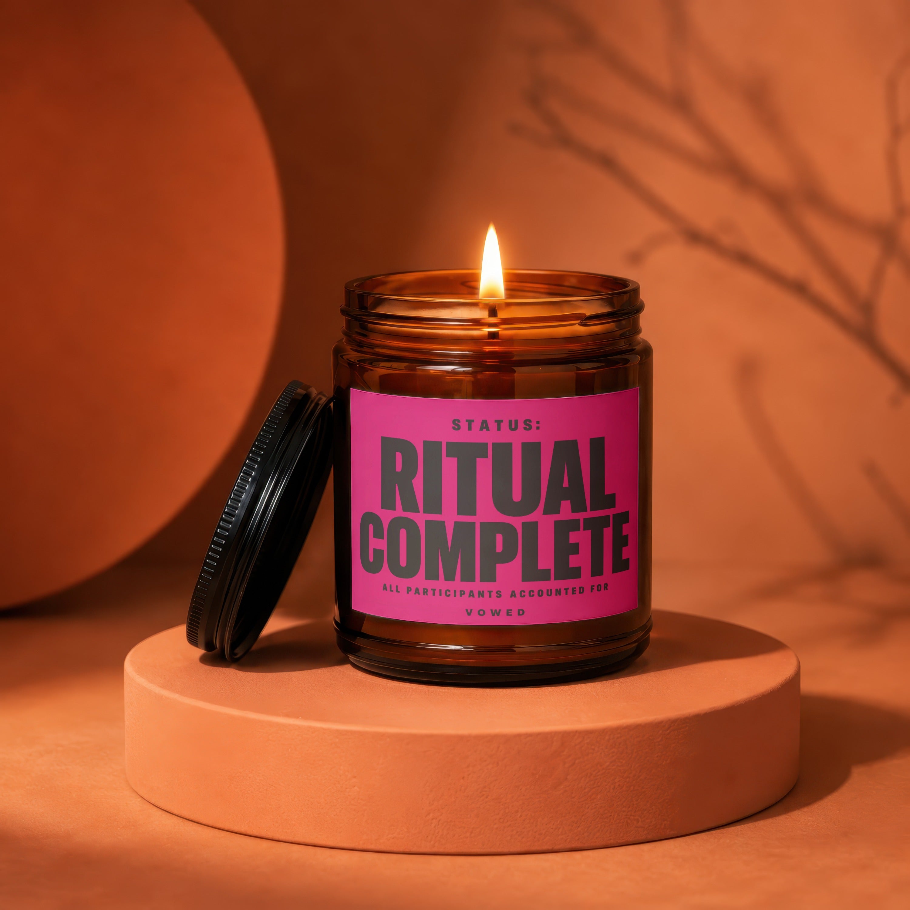 Amber jar candle with pink label reading "STATUS: RITUAL COMPLETE"
