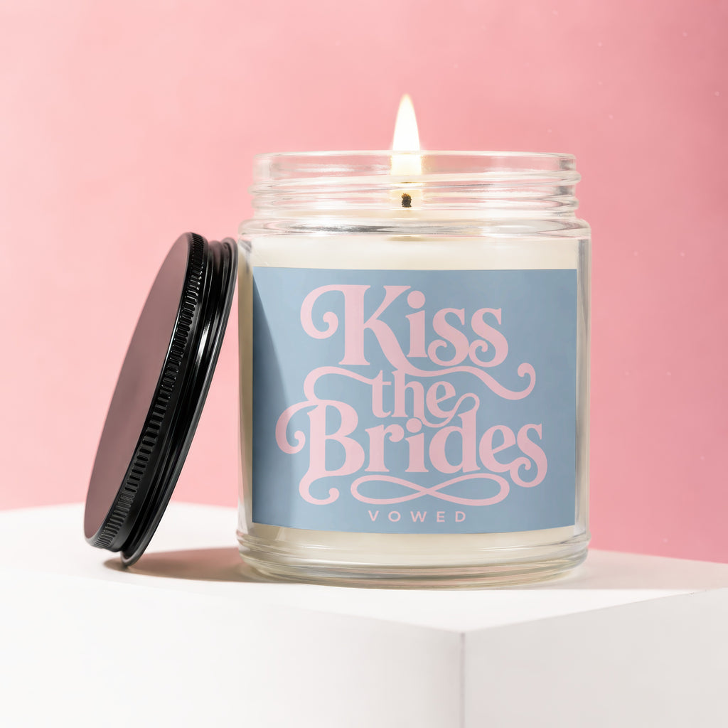 Glass jar candle with black lid, inscribed "Kiss the Brides VOWED" in pink script.