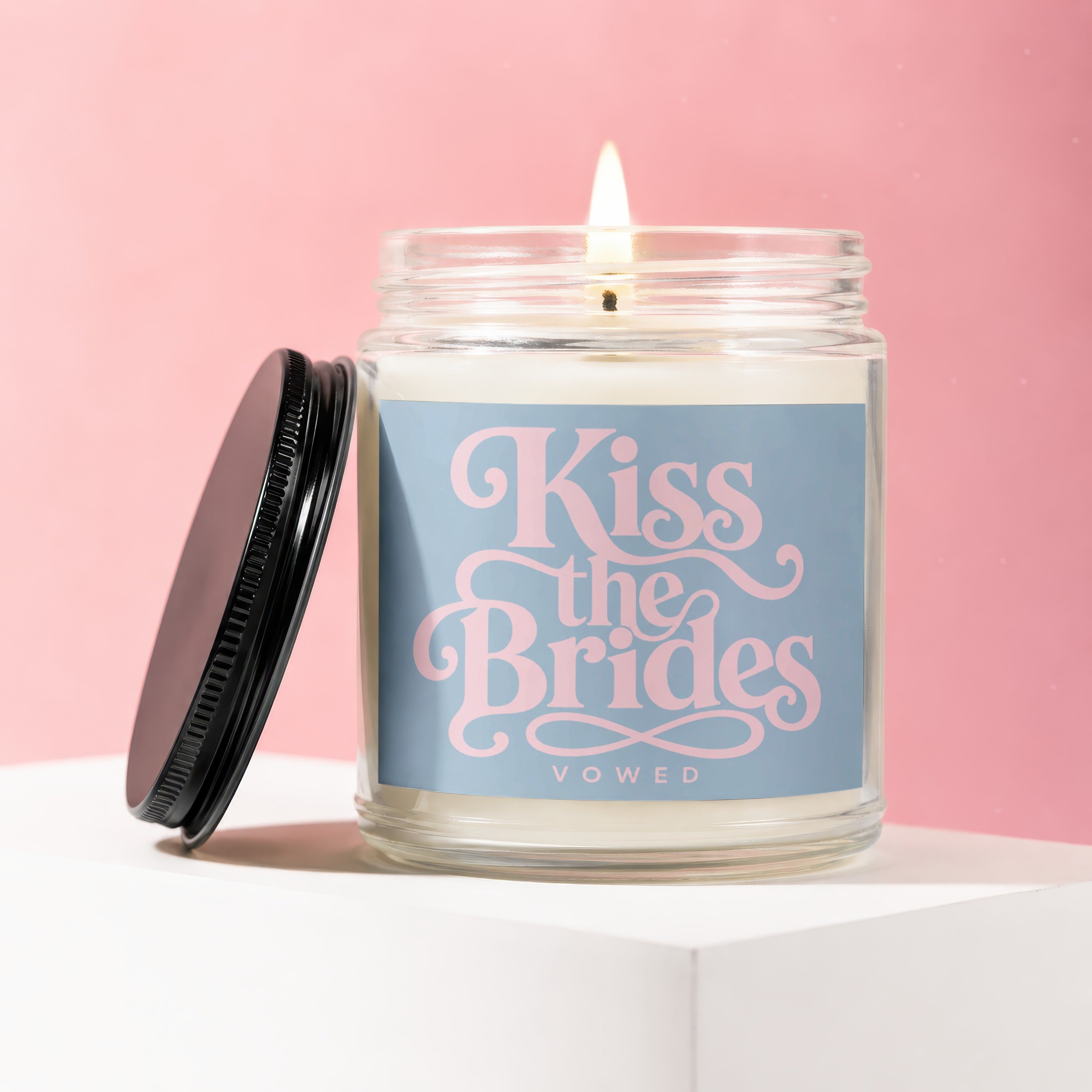Glass jar candle with black lid, inscribed "Kiss the Brides VOWED" in pink script.