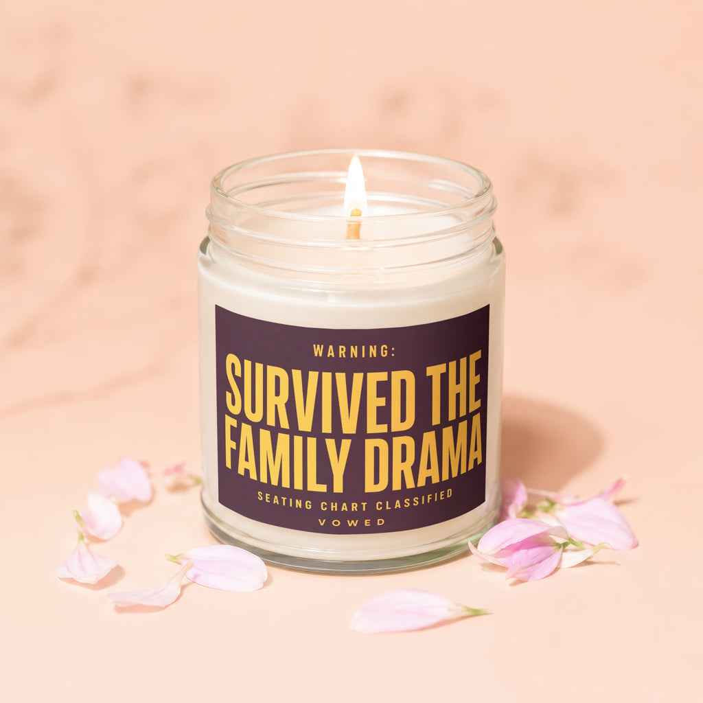 Candle with label "Warning: Survived The Family Drama" and scattered pink petals.