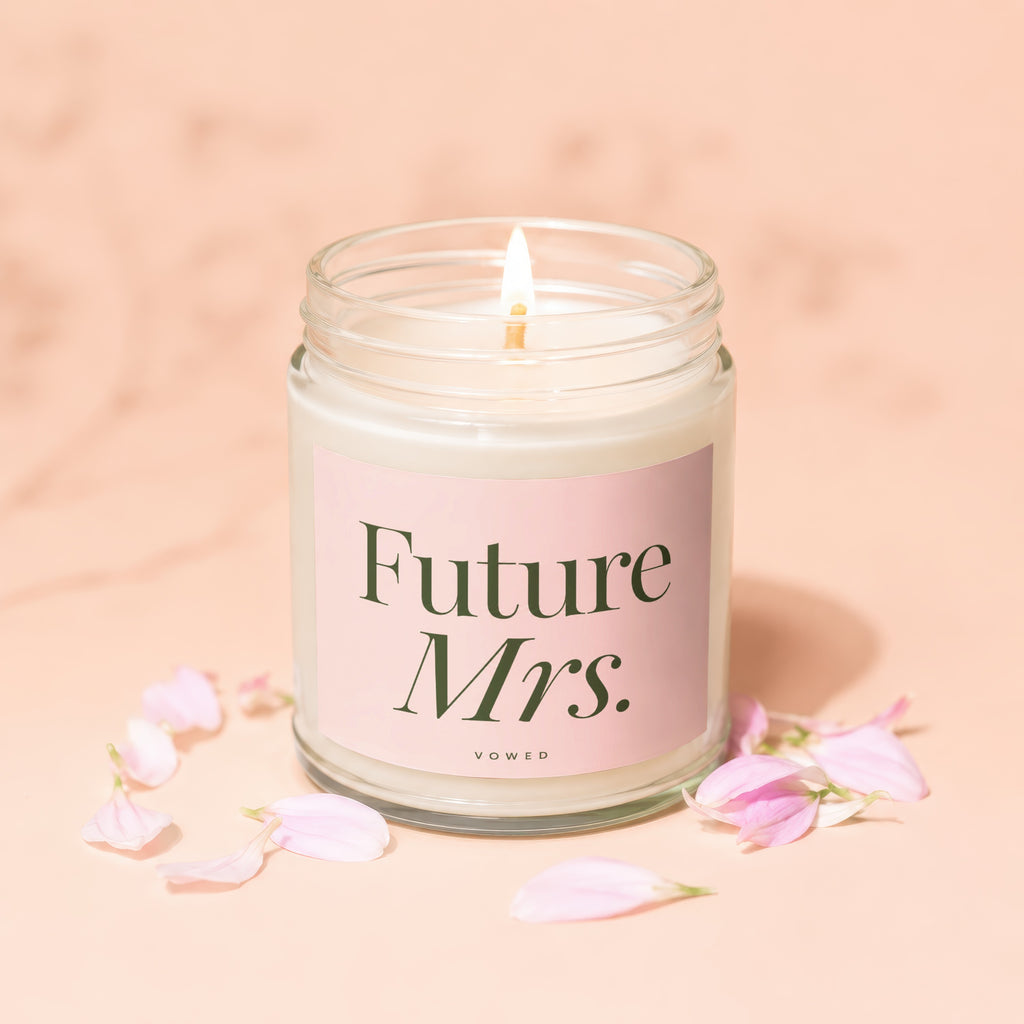A lit jar candle with a "Future Mrs." label, surrounded by pink petals.
