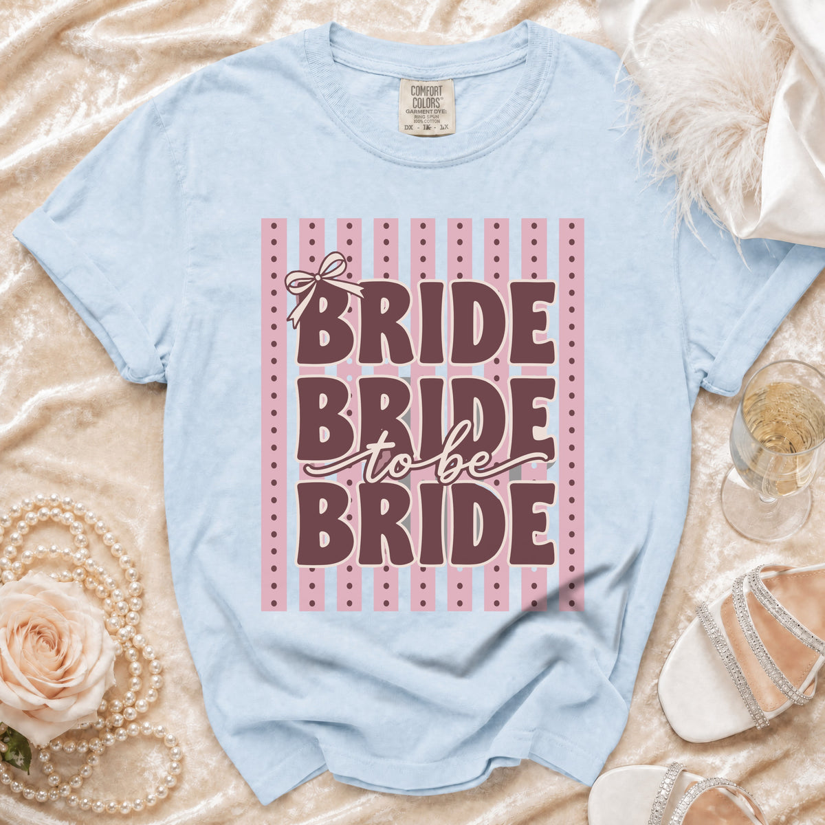 Light blue t-shirt with "BRIDE to be BRIDE" text and pink stripe background.
