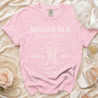 Pink t-shirt with "Reckless in Texas Olivia's Bach" and disco boot design.
