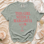 A sage graphic tee with "THIS GIRL NEEDS A MARGARITA" and a margarita glass.