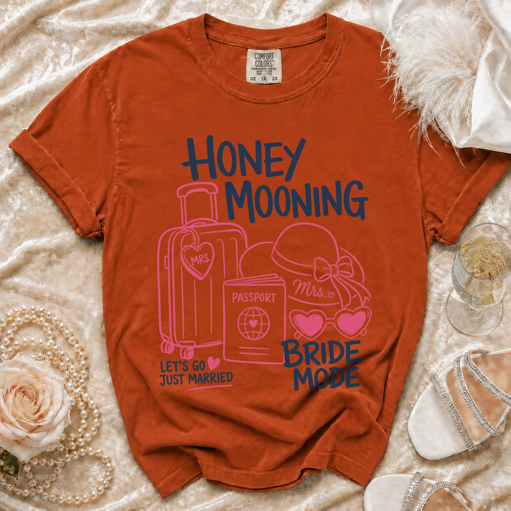 Orange t-shirt with "Honey Mooning Bride Mode" graphic, suitcase, passport, hat, glasses.