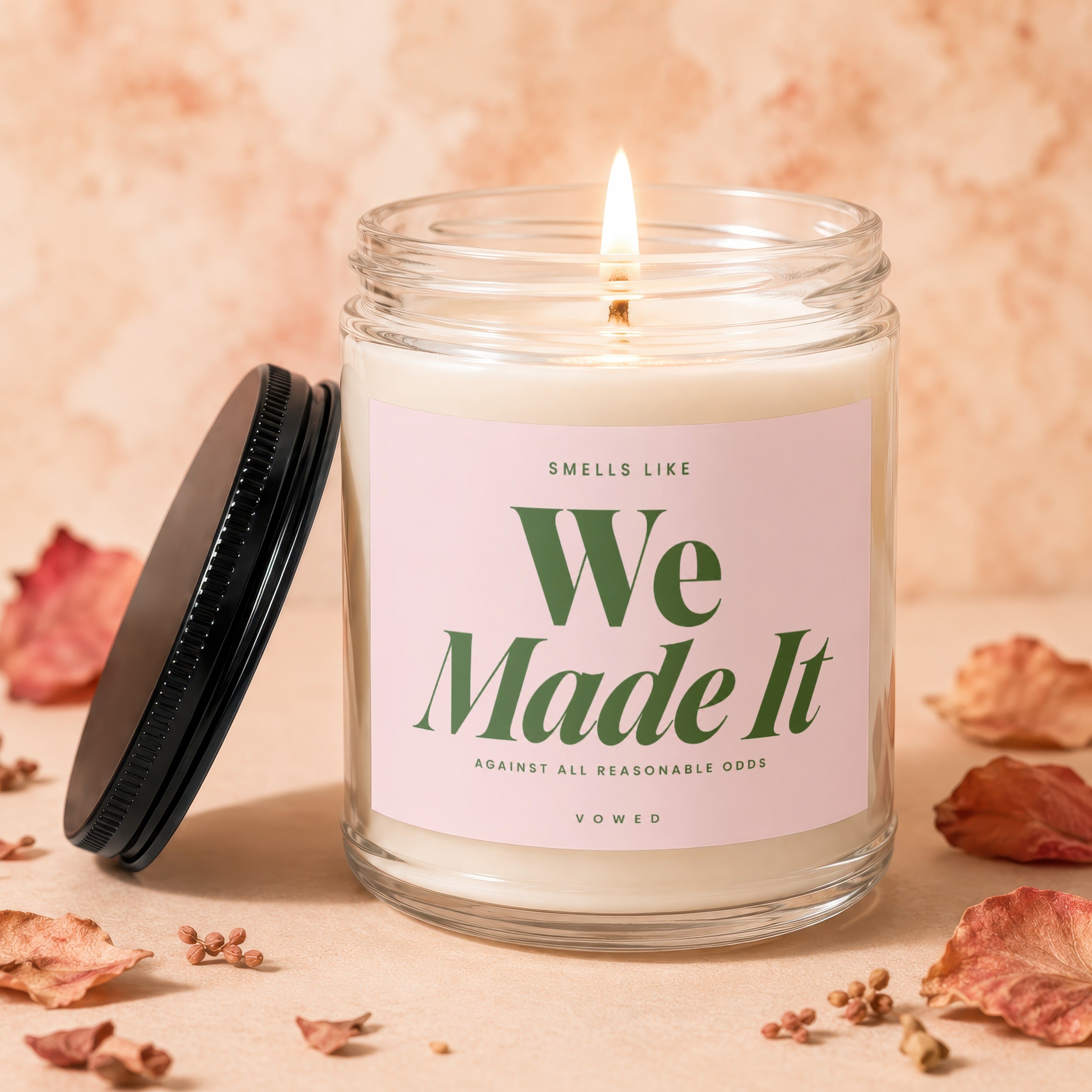 Candle with lit wick features text "Smells Like We Made It Against All Reasonable Odds".