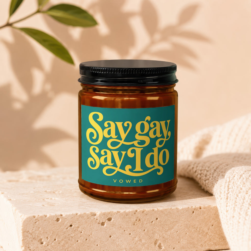 Amber jar candle with black lid, features teal label with yellow text "Say gay Say I do VOWED".