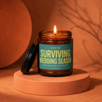 Amber jar candle with burning flame and label that reads "Surviving Wedding Season".
