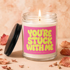 Glass candle with lit wick and pink label reading "YOU'RE STUCK WITH ME".