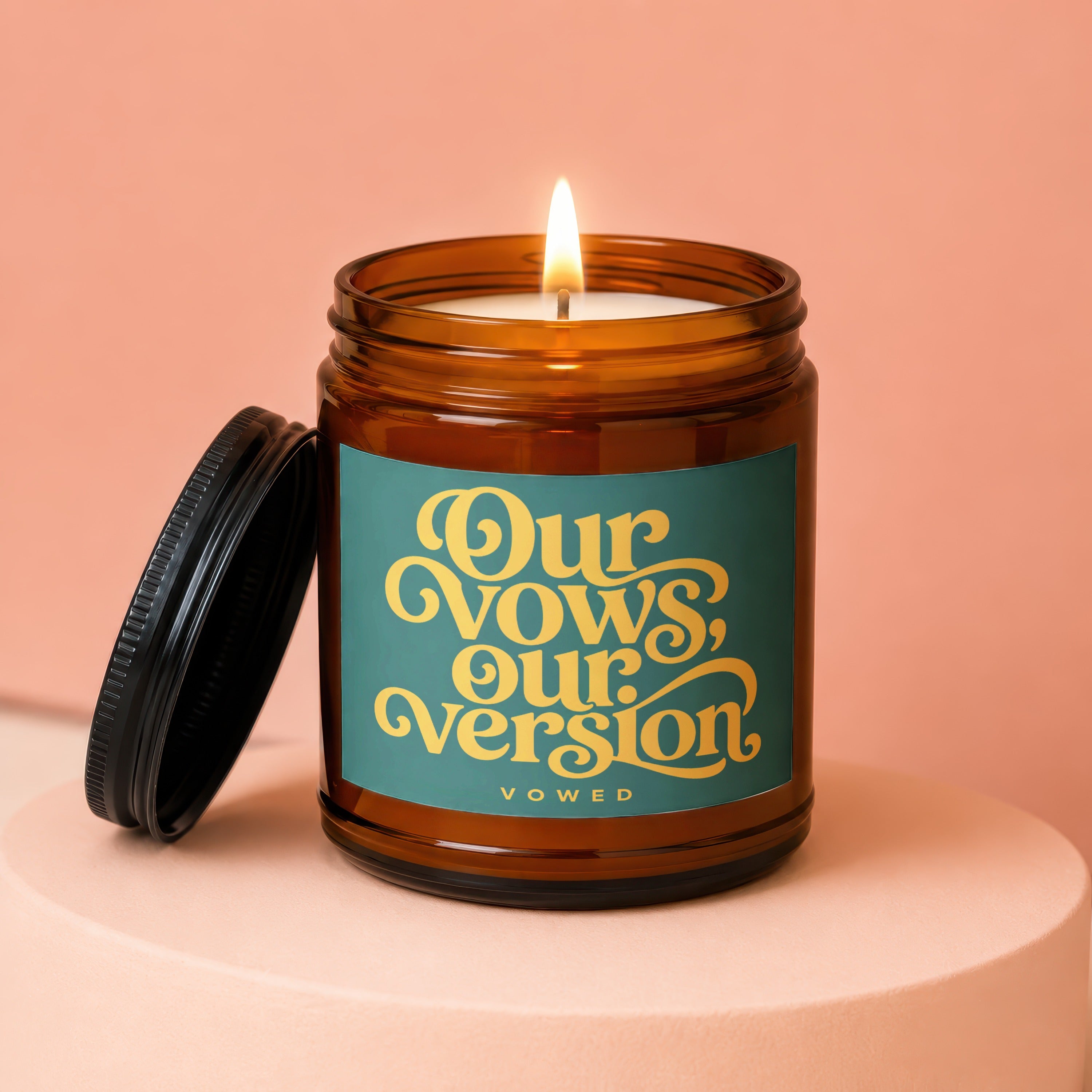 Amber glass candle with lit flame and teal label reading "Our Vows, Our Version. Vowed."