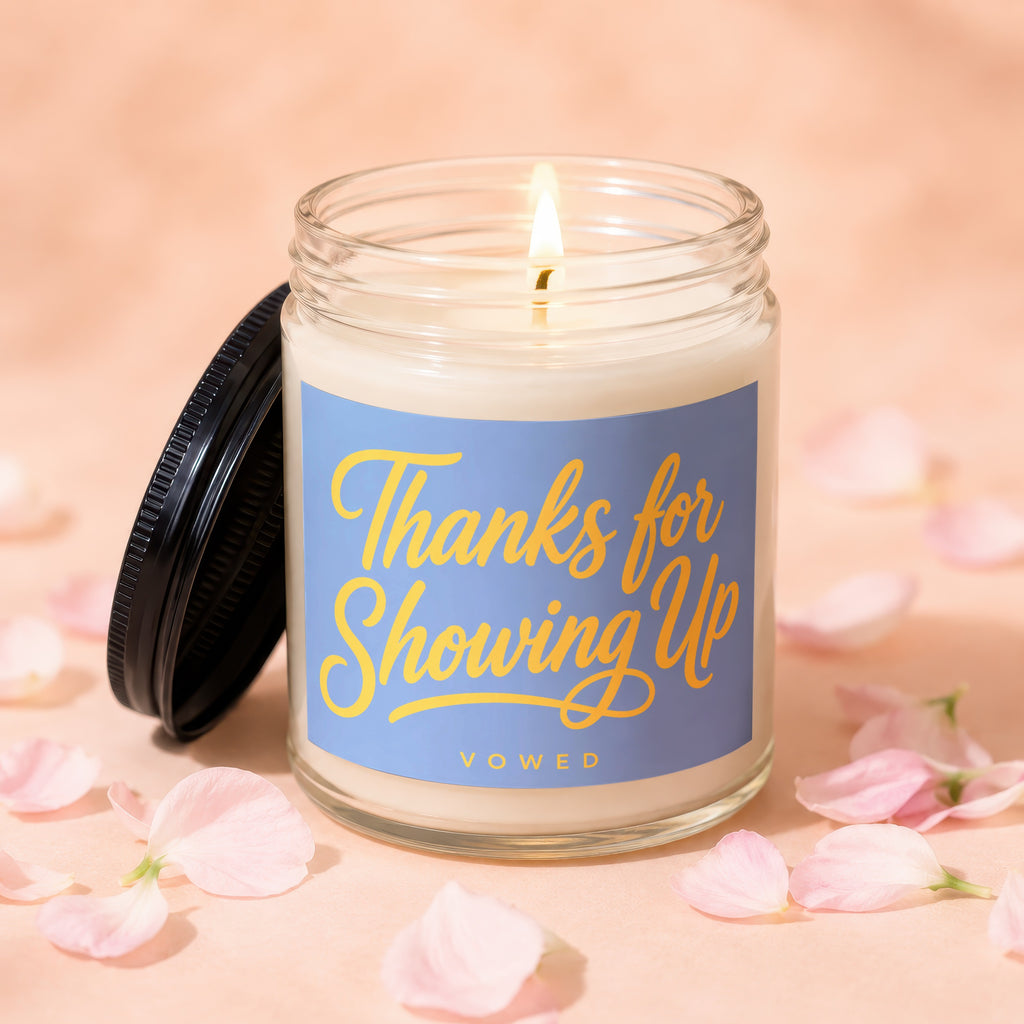 Glass candle with lit wick, blue label reading "Thanks for Showing Up" and "VOWED".
