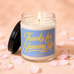 Glass candle with lit wick, blue label reading "Thanks for Showing Up" and "VOWED".