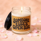Scented candle with "Smells Like Someone Else's Open Bar" on label surrounded by pink petals.