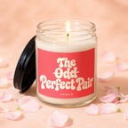 Candle labeled "The Odd Perfect Pair VOWED" with lid off and lit wick, surrounded by petals.