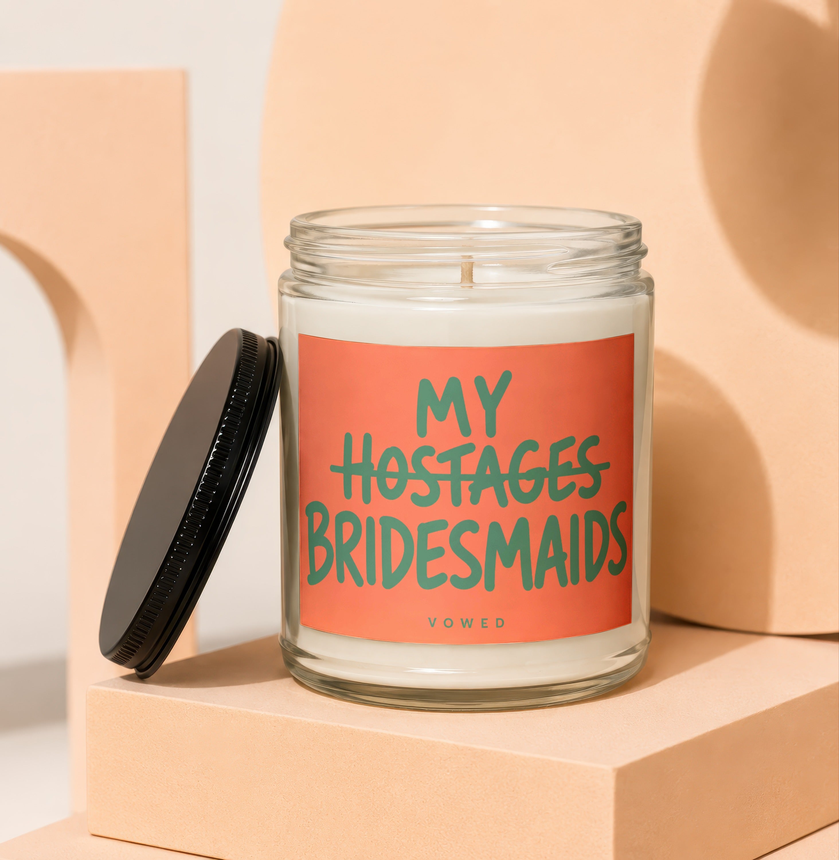 Glass candle with "My Hostages Bridesmaids" text on coral label.