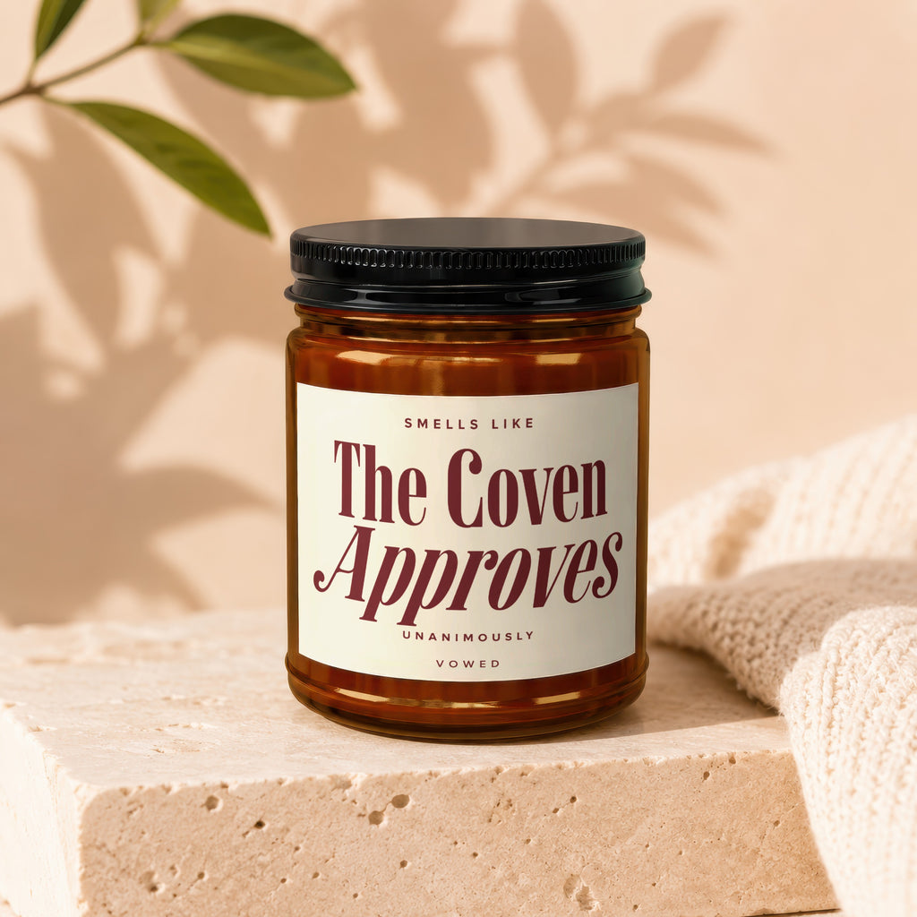Amber candle with a label that reads "Smells Like The Coven Approves," "Unanimously," and "Vowed."