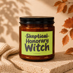Amber glass candle with "Skeptical Honorary Witch" text on a lime green label.