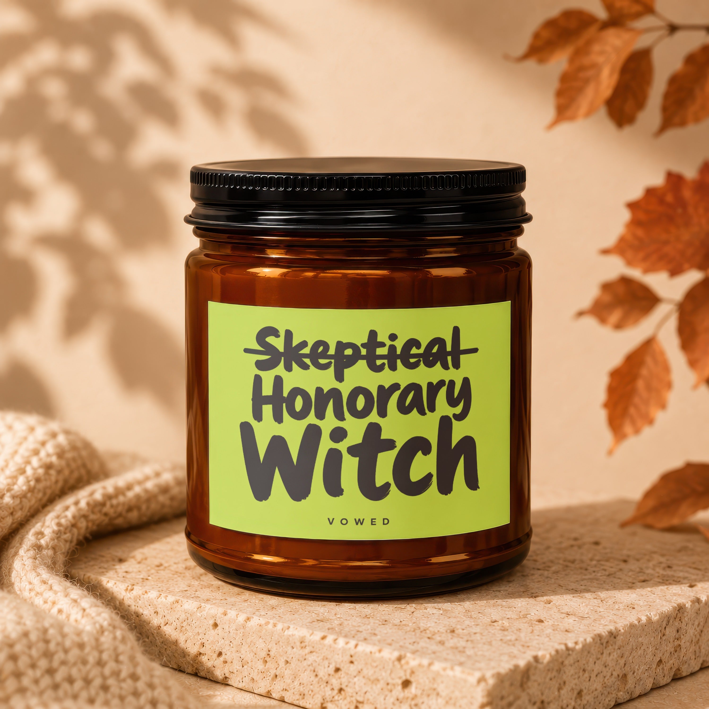 Amber glass candle with "Skeptical Honorary Witch" text on a lime green label.