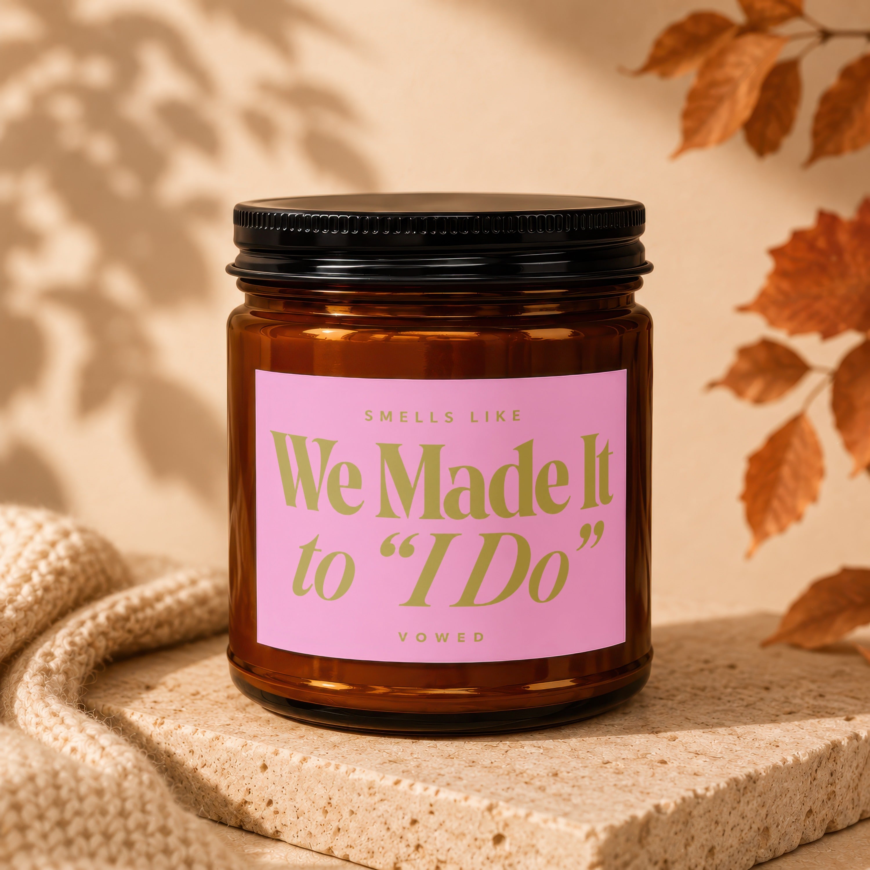 Amber glass candle with pink label reading "Smells like We Made It to 'I Do'"