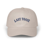 Light tan baseball cap with "LAST TOAST" embroidered in navy blue.